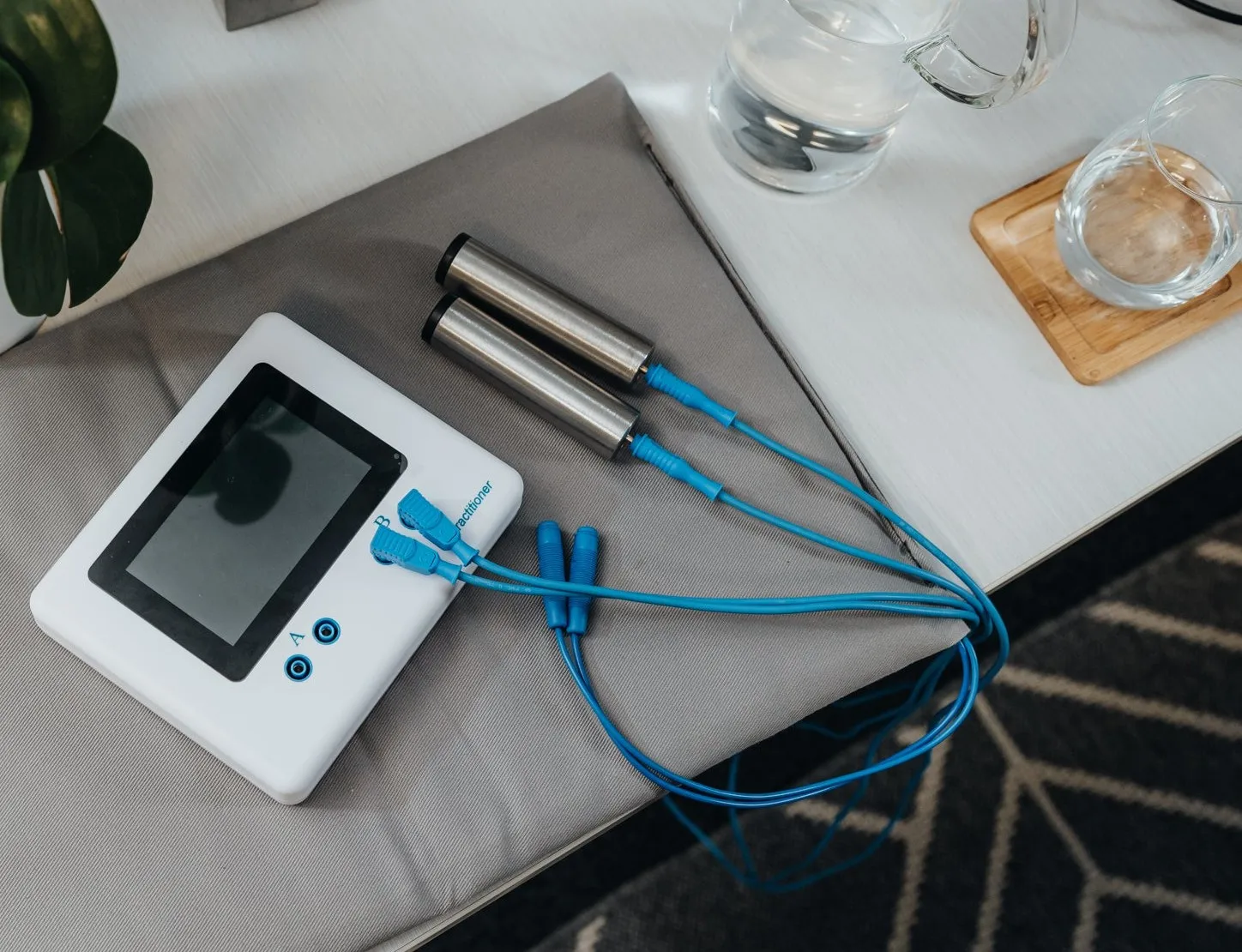 The Qrife unit with its screen, two stainless steel hand rods on blue leads, resting on the grey PEMF coil pad